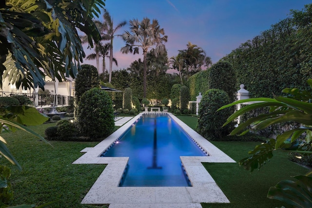 pool at dusk featuring a lawn