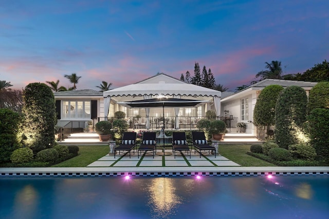 back house at dusk featuring a water view and a patio