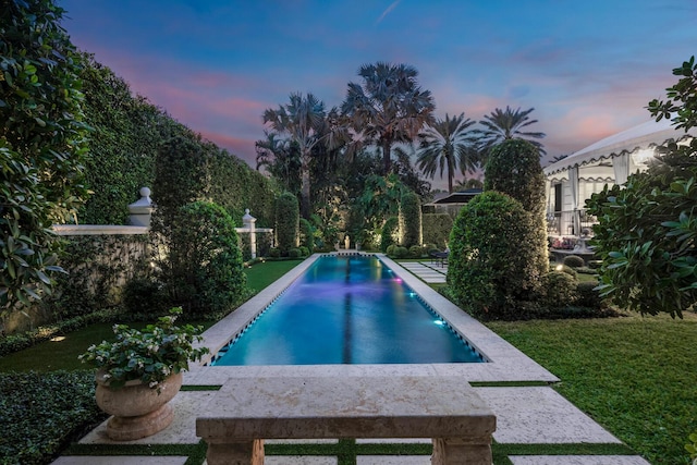 pool at dusk featuring a lawn