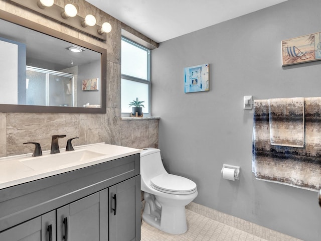 bathroom featuring tile patterned floors, toilet, a shower with shower door, vanity, and backsplash