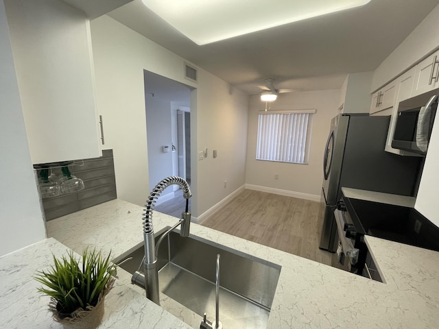 kitchen featuring white cabinetry, sink, light stone counters, light hardwood / wood-style flooring, and appliances with stainless steel finishes