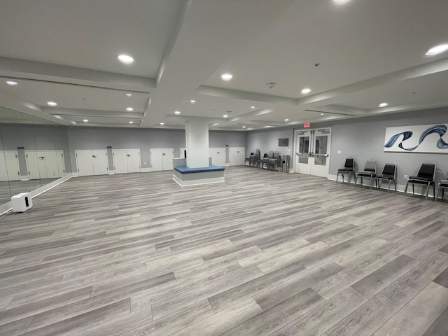 gym with french doors, light hardwood / wood-style floors, and a raised ceiling