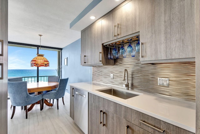 kitchen with backsplash, pendant lighting, stainless steel dishwasher, sink, and a water view