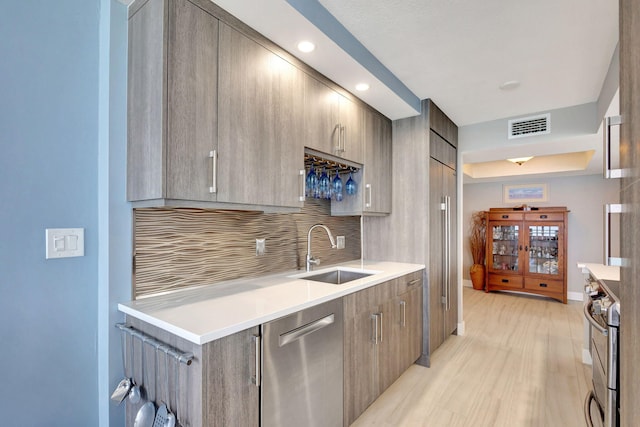 kitchen featuring appliances with stainless steel finishes, light hardwood / wood-style floors, backsplash, and sink