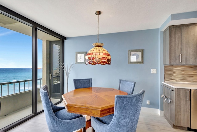 dining area featuring a water view, light wood-type flooring, plenty of natural light, and a textured ceiling