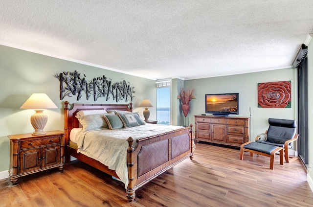 bedroom featuring wood-type flooring, ornamental molding, and a textured ceiling