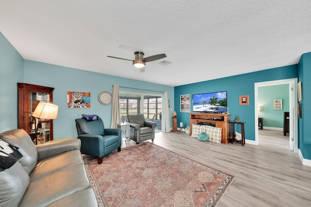 living room featuring ceiling fan, a textured ceiling, and light wood-type flooring