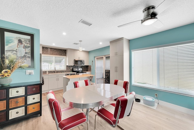 dining space featuring ceiling fan, sink, a textured ceiling, and light hardwood / wood-style floors