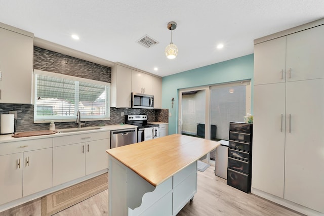 kitchen with appliances with stainless steel finishes, a kitchen island, sink, backsplash, and hanging light fixtures