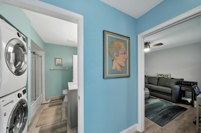 laundry area with ceiling fan, a textured ceiling, stacked washing maching and dryer, and light wood-type flooring