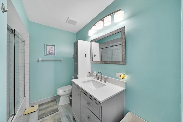 bathroom with hardwood / wood-style floors, toilet, vanity, and a tile shower