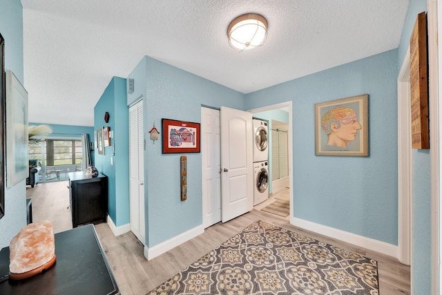 hallway with a textured ceiling, stacked washer / drying machine, and light hardwood / wood-style flooring