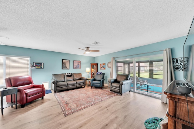 living room featuring ceiling fan, light wood-type flooring, and a textured ceiling