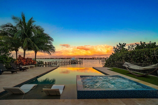 pool at dusk with a jacuzzi, a patio, and a water view