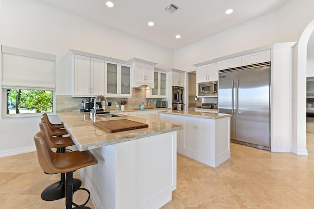 kitchen featuring sink, a center island, light stone counters, kitchen peninsula, and built in appliances