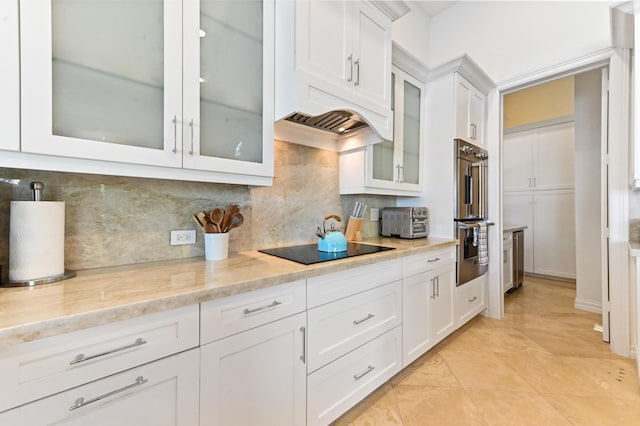 kitchen with decorative backsplash, black electric stovetop, light stone counters, stainless steel double oven, and white cabinetry