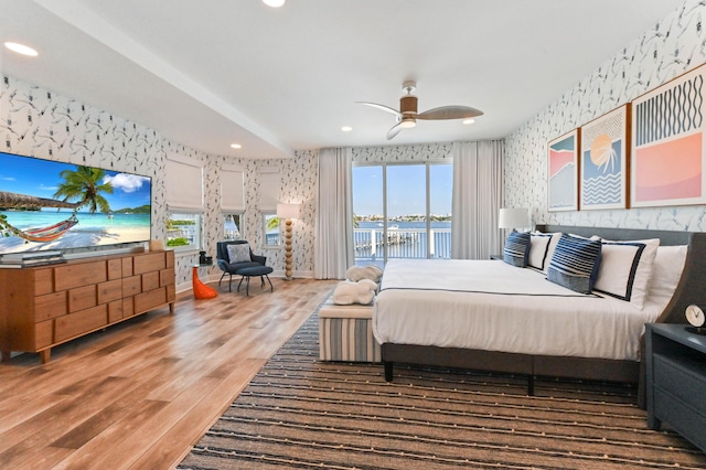 bedroom with access to outside, a water view, ceiling fan, and hardwood / wood-style floors