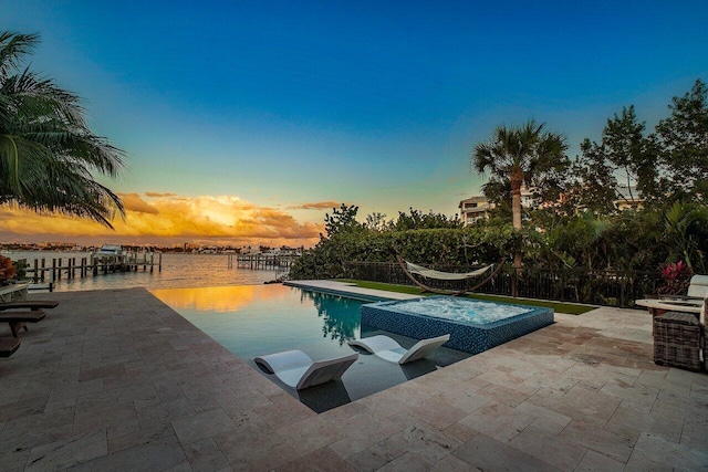 pool at dusk featuring a patio area, an in ground hot tub, and a water view