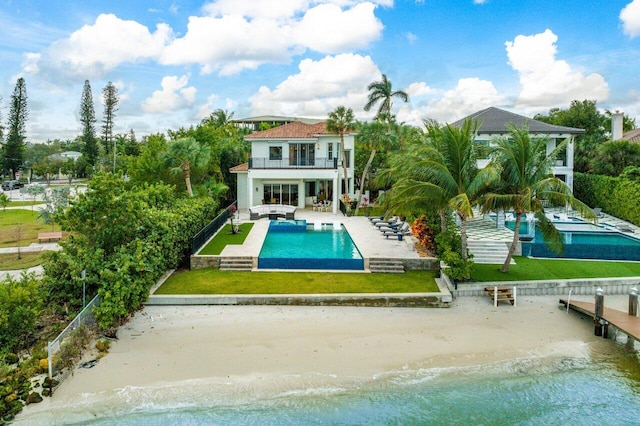 rear view of house with a balcony, a water view, a patio area, a beach view, and a lawn