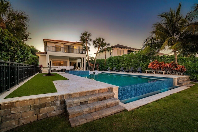 pool at dusk featuring a patio, an outdoor hangout area, and a lawn