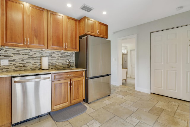 kitchen with backsplash, light stone countertops, sink, and appliances with stainless steel finishes