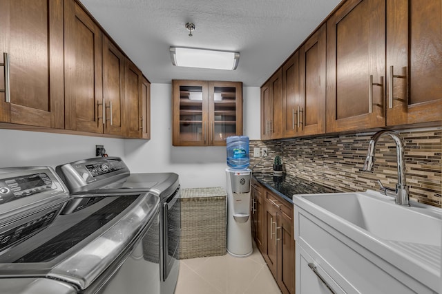 laundry area with a textured ceiling, washing machine and dryer, cabinets, sink, and light tile patterned floors