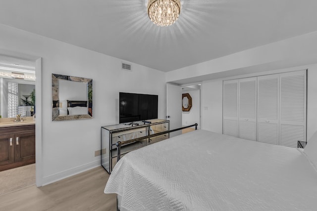 bedroom featuring light wood-type flooring, an inviting chandelier, sink, and ensuite bath