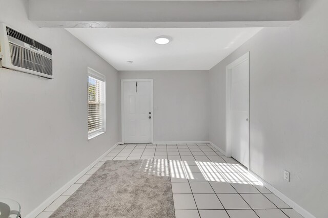 empty room with an AC wall unit, beamed ceiling, and light tile patterned floors