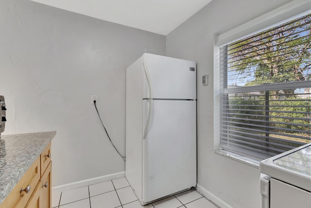 kitchen with light tile patterned floors, white refrigerator, and light brown cabinetry