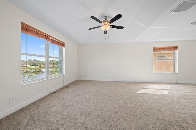 spare room with light carpet, ceiling fan, a water view, and a tray ceiling