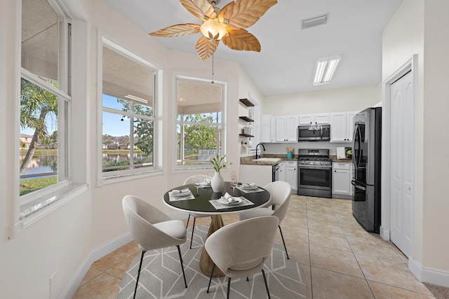 tiled dining room with ceiling fan, a water view, vaulted ceiling, and sink