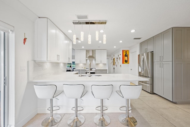 kitchen with kitchen peninsula, stainless steel fridge, gray cabinets, wall chimney range hood, and pendant lighting