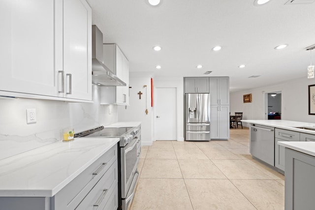 kitchen with light tile patterned floors, stainless steel appliances, gray cabinetry, decorative light fixtures, and wall chimney range hood