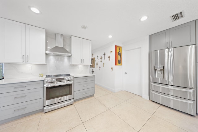 kitchen with light tile patterned floors, stainless steel appliances, wall chimney exhaust hood, and white cabinets