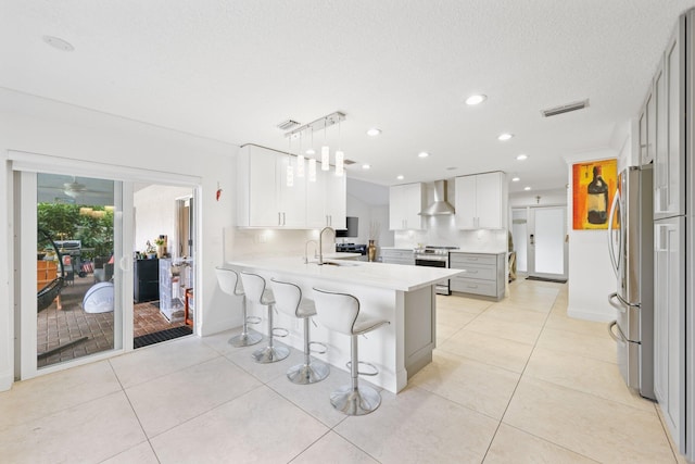 kitchen with white cabinetry, kitchen peninsula, appliances with stainless steel finishes, hanging light fixtures, and wall chimney range hood