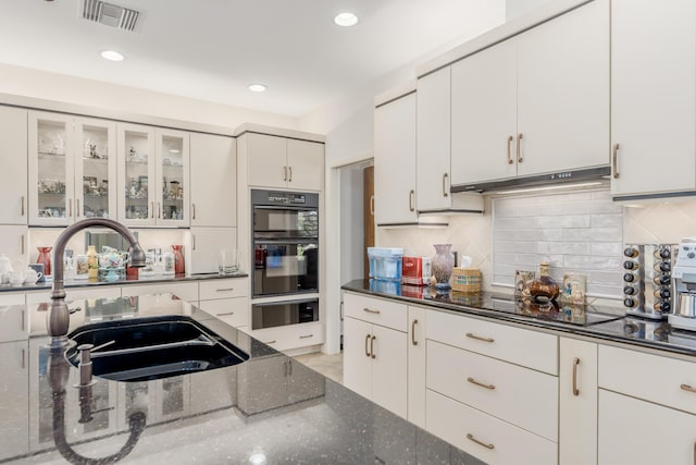 kitchen featuring tasteful backsplash, sink, black appliances, dark stone countertops, and white cabinets