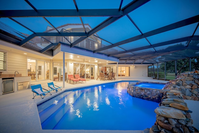 view of swimming pool featuring an in ground hot tub, an outdoor kitchen, a lanai, ceiling fan, and a patio area