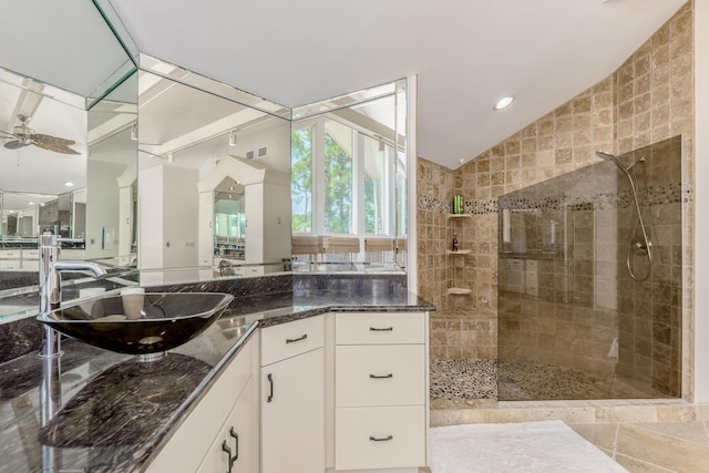 bathroom featuring ceiling fan, vanity, vaulted ceiling, and tiled shower