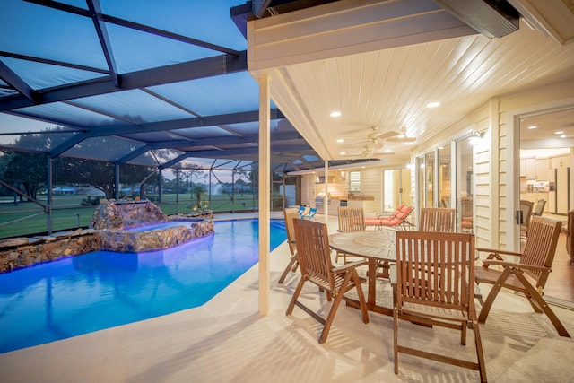 pool at dusk featuring a lanai, pool water feature, ceiling fan, a patio area, and a hot tub