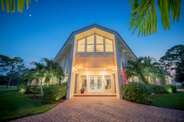 back house at dusk with a lawn and french doors