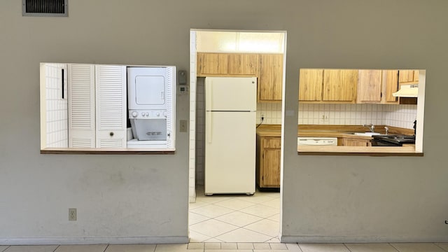 kitchen featuring sink, backsplash, light tile patterned floors, stacked washer and clothes dryer, and white appliances