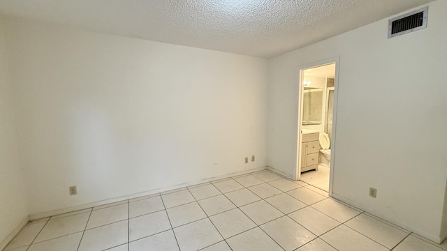 unfurnished bedroom with light tile patterned flooring, a textured ceiling, and connected bathroom