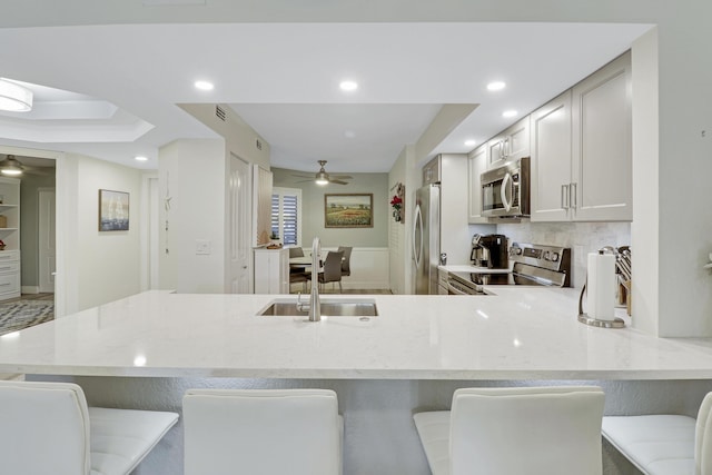 kitchen featuring sink, backsplash, kitchen peninsula, a breakfast bar area, and appliances with stainless steel finishes