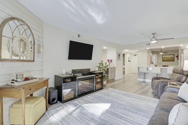 living room with light wood-type flooring, ceiling fan, and wood walls