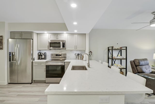 kitchen featuring kitchen peninsula, light wood-type flooring, stainless steel appliances, sink, and gray cabinets