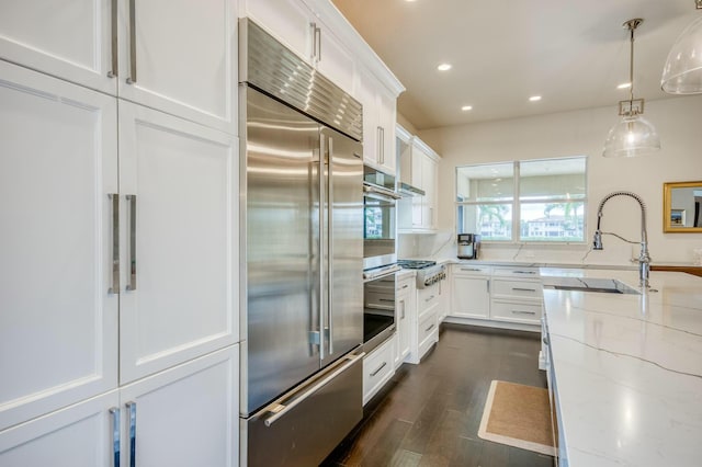 kitchen featuring light stone countertops, appliances with stainless steel finishes, white cabinets, and decorative light fixtures