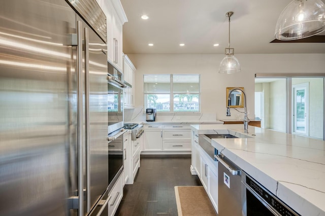 kitchen with pendant lighting, sink, white cabinetry, light stone countertops, and stainless steel appliances