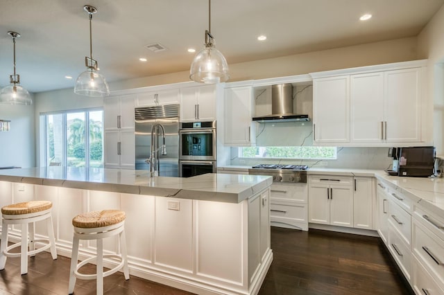 kitchen with stainless steel appliances, tasteful backsplash, light stone countertops, white cabinets, and wall chimney range hood