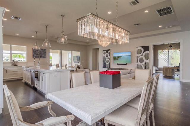 dining space featuring dark wood-type flooring, a tray ceiling, and a chandelier