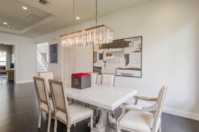 dining room featuring dark hardwood / wood-style flooring, a raised ceiling, and a notable chandelier